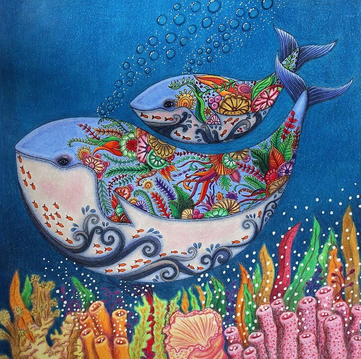 The finished whale page: two pale blue whales with pink bellies and dark blue waves, their backs full of colorful flowers, shells and leaves, above orange, green and pink corals, with white bubbles rising through a deep blue ocean