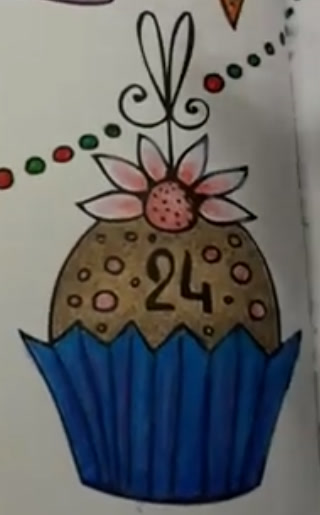 Colored pencil cupcake numbered 24 from Rita Berman’s advent calendar page: golden brown cake with pink dots in a blue paper cup, a pink flower and a hanging ribbon on top